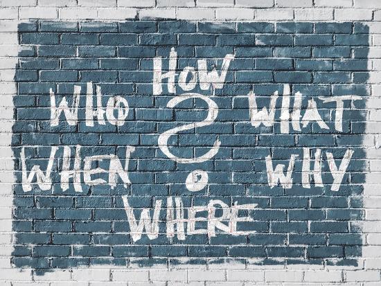 The words who, how, what, why, where, and when painted on a brick wall with a question mark in the center.