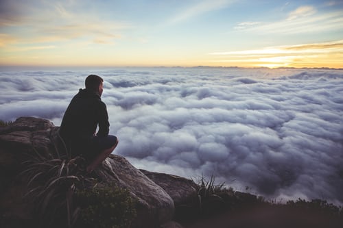 A man on a mountain looking over the clouds that blanket the view.