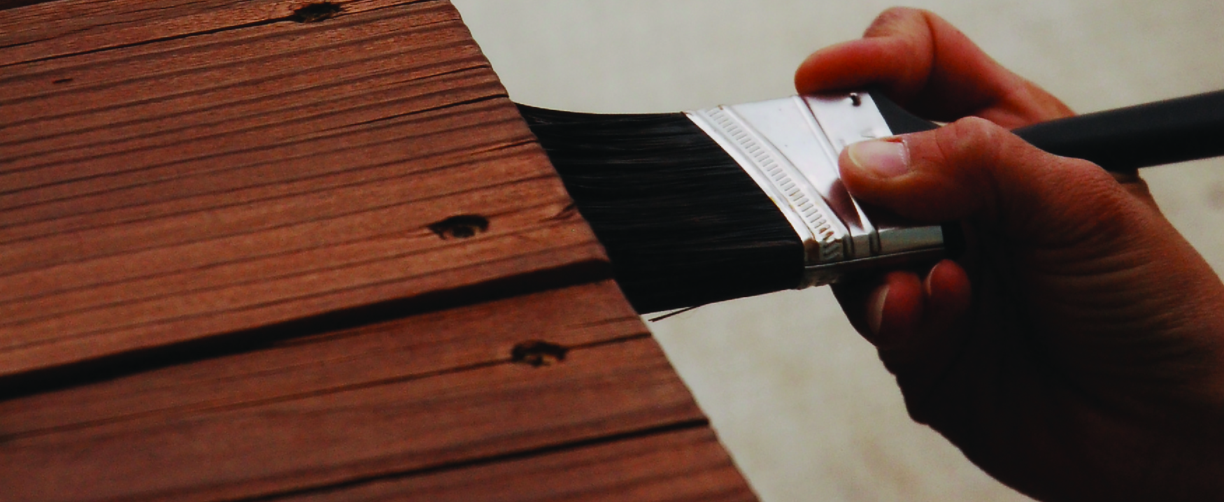 A photograph shows someone holding a brush applying stain to a piece of wood furniture.