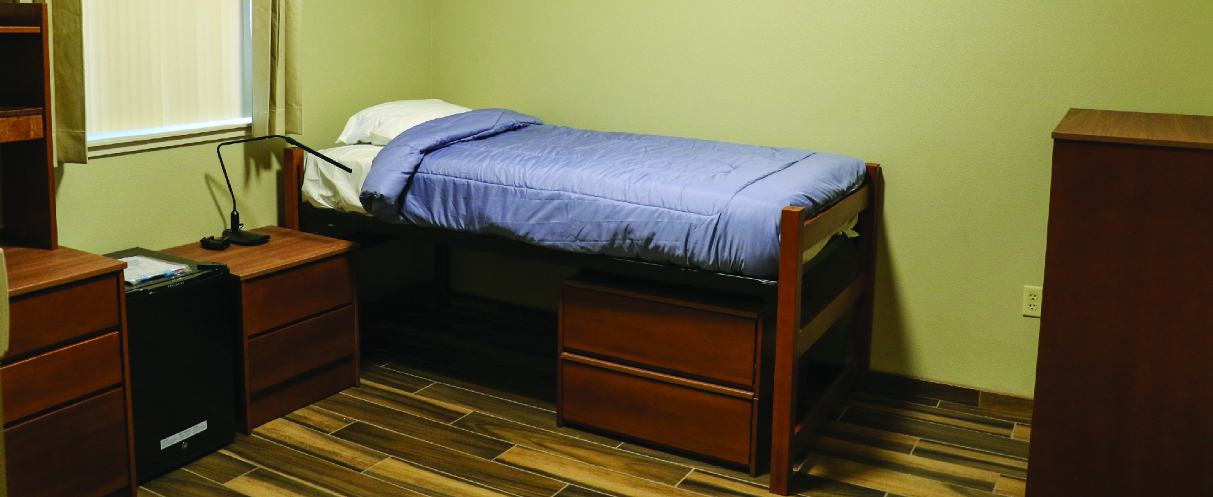 A photograph shows a dorm room with a bed and matching furniture.