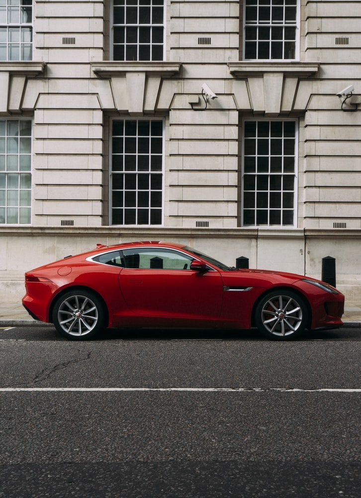 A red Jaguar car sits on the street in front of a building.