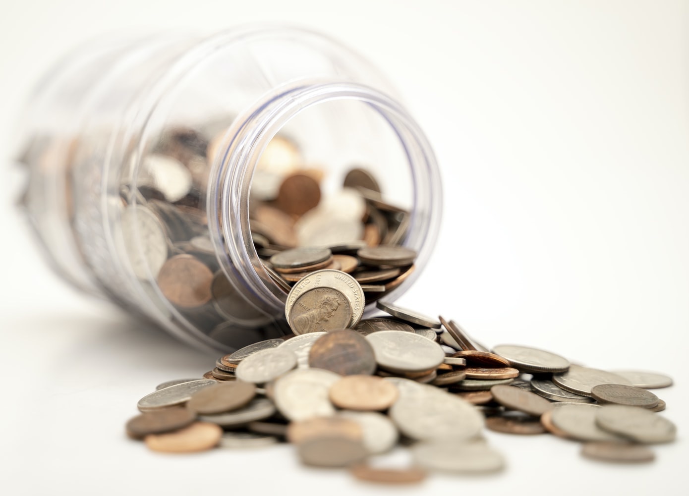 Coins spilling out of a mason jar on a white table.